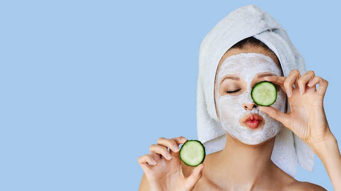 Beautiful young woman with facial mask on her face holding slices of cucumber.